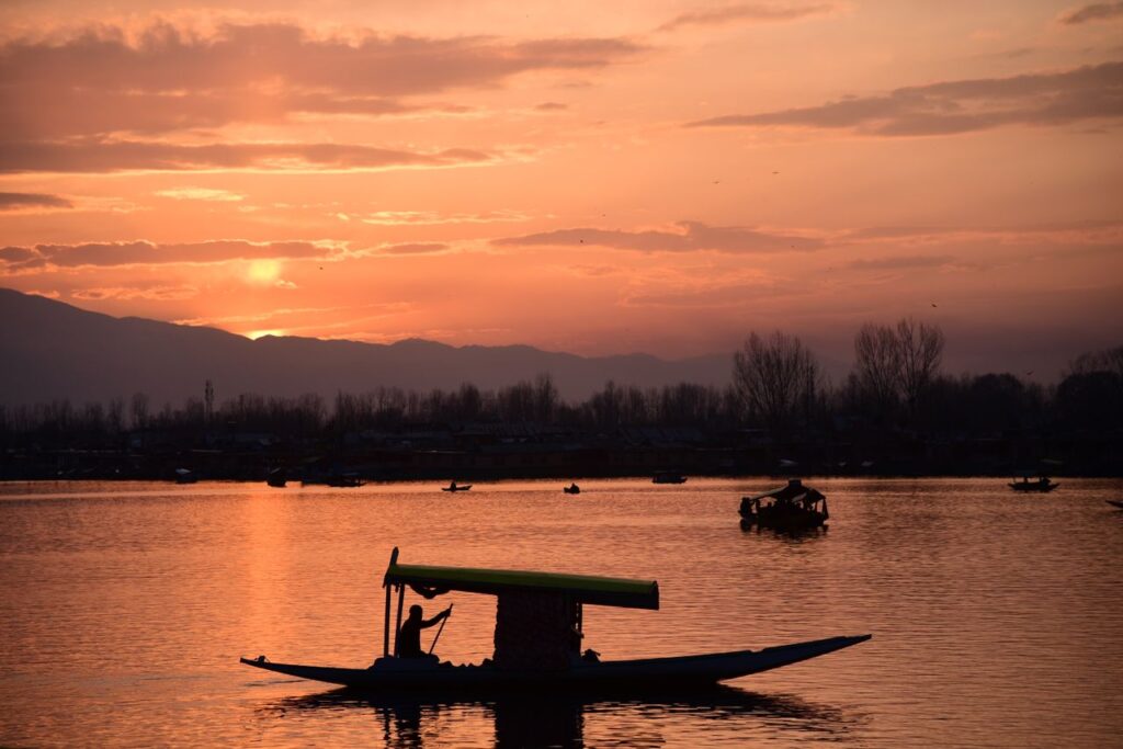A stunning sunset over Dal Lake in Srinagar, featuring a silhouette of a traditional Shikara boat.