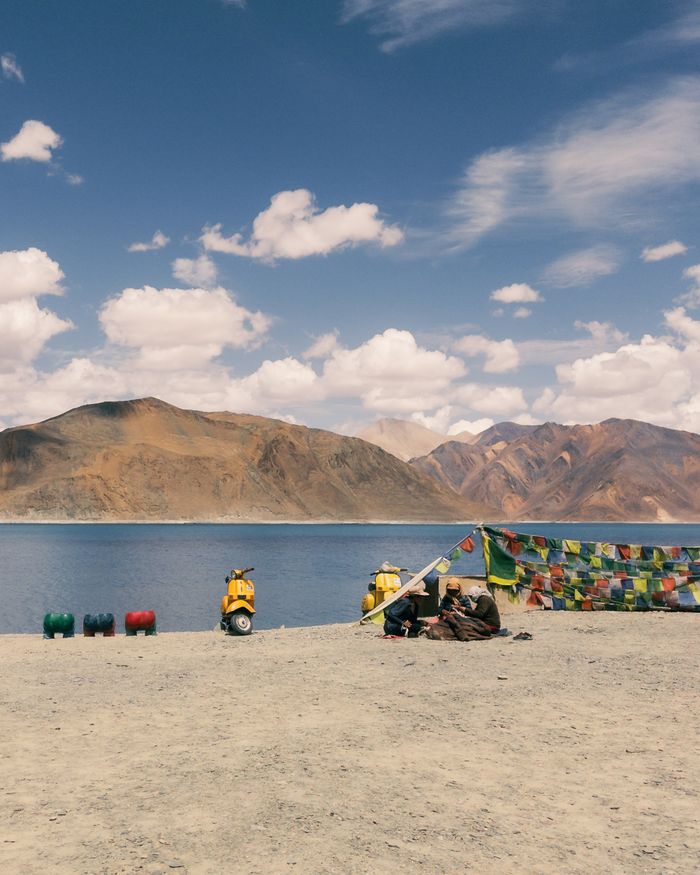 Tranquil view of Pangong Lake in Ladakh, India, with vibrant prayer flags and distant mountains.
